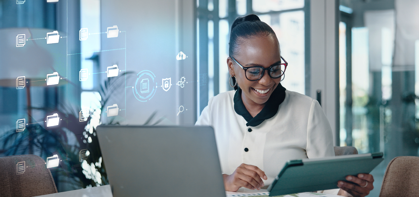 A woman is working at her desk as icons relating to document management appear next to her. She is reviewing a smart tablet held in her hand.