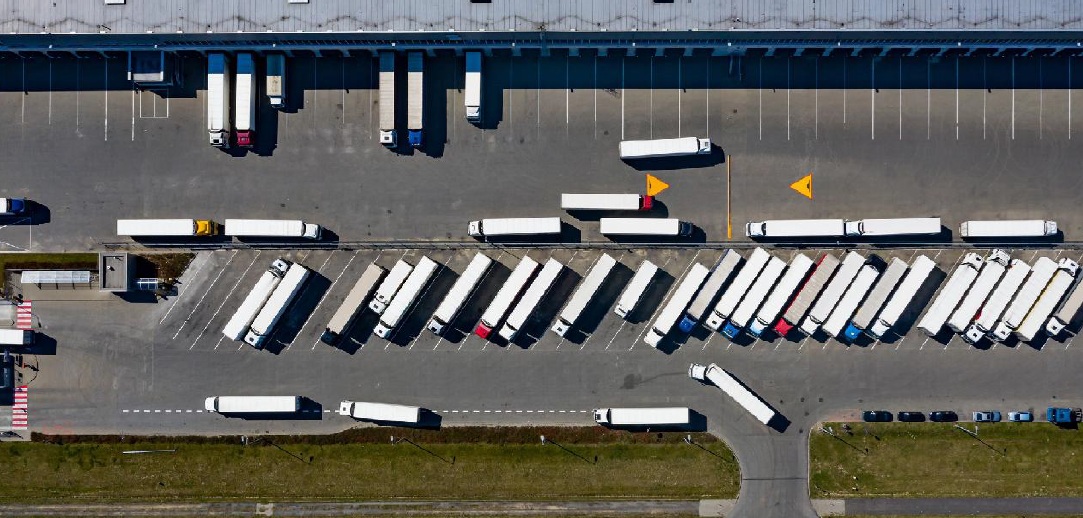 Aerial view of a logistics distribution center with multiple trucks and trailers parked at loading docks and maneuvering through the yard.