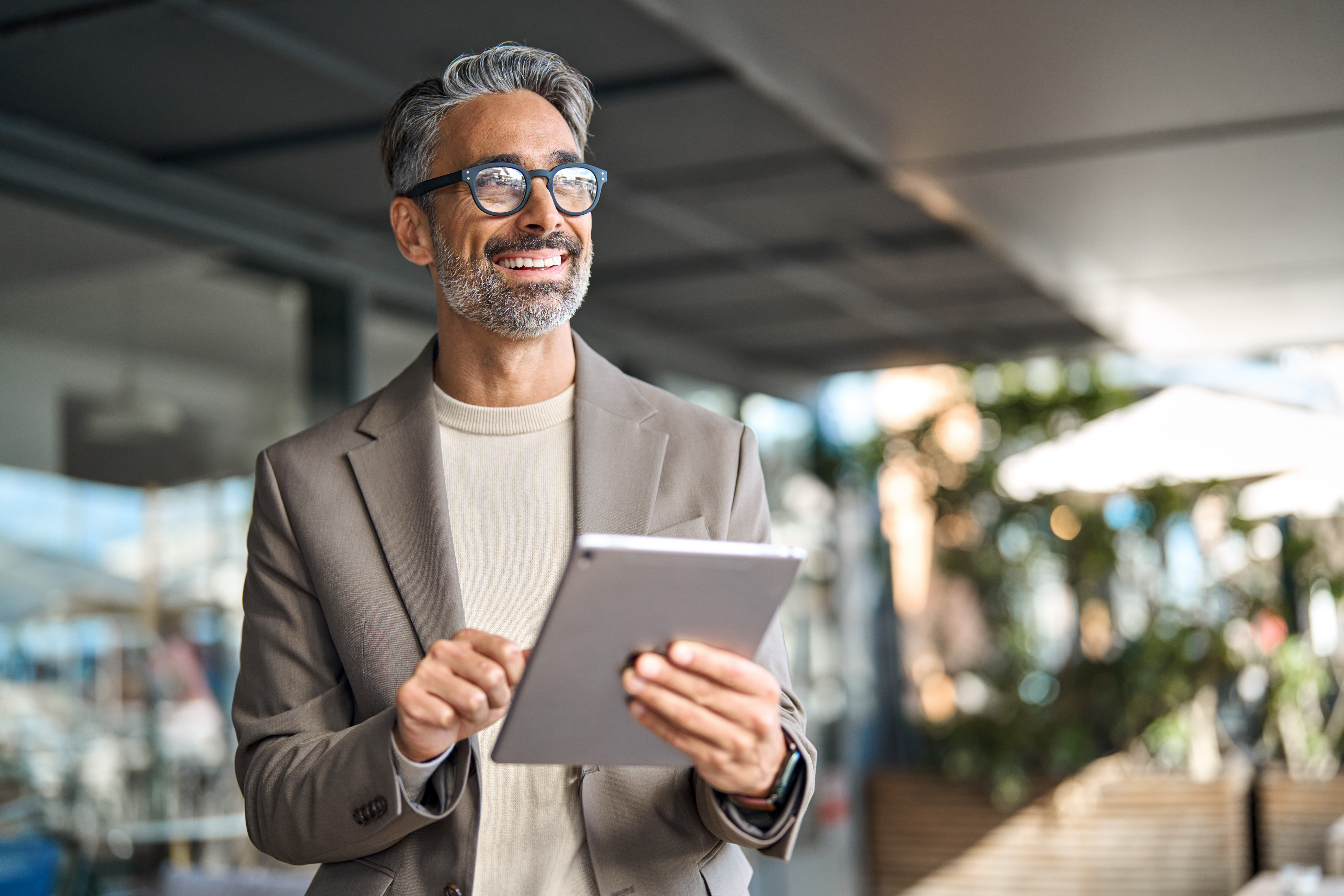 Smiling man with gray hair and glasses holding a tablet