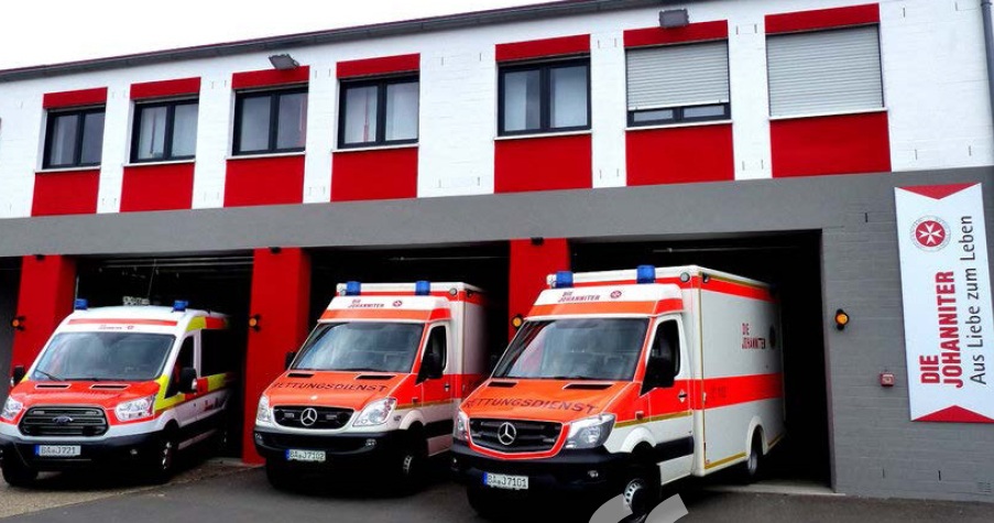 Three Johanniter ambulances parked in garage bays of a red and white emergency services building