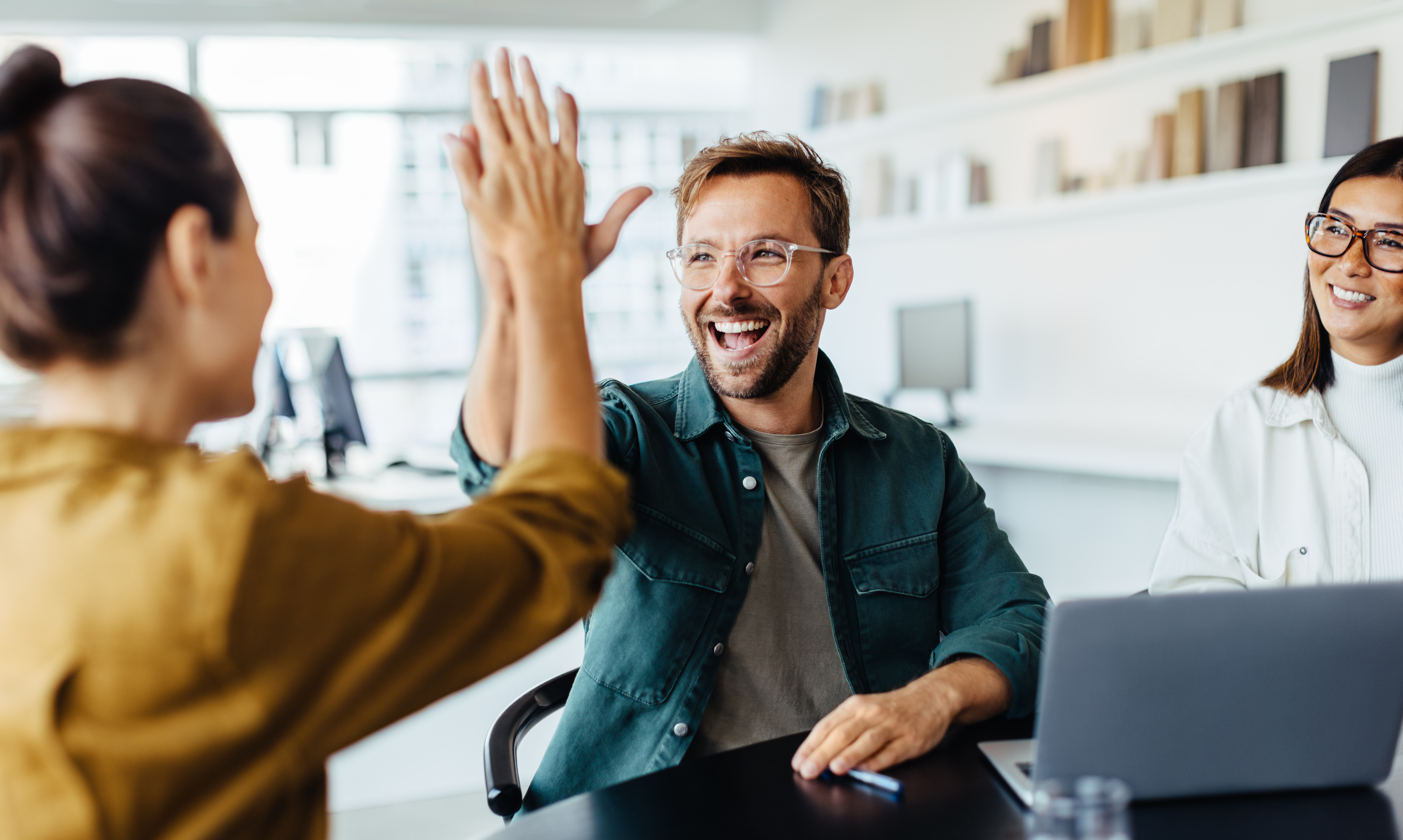 Team members giving a high-five during a collaborative office meeting, representing teamwork, productivity and workplace success.