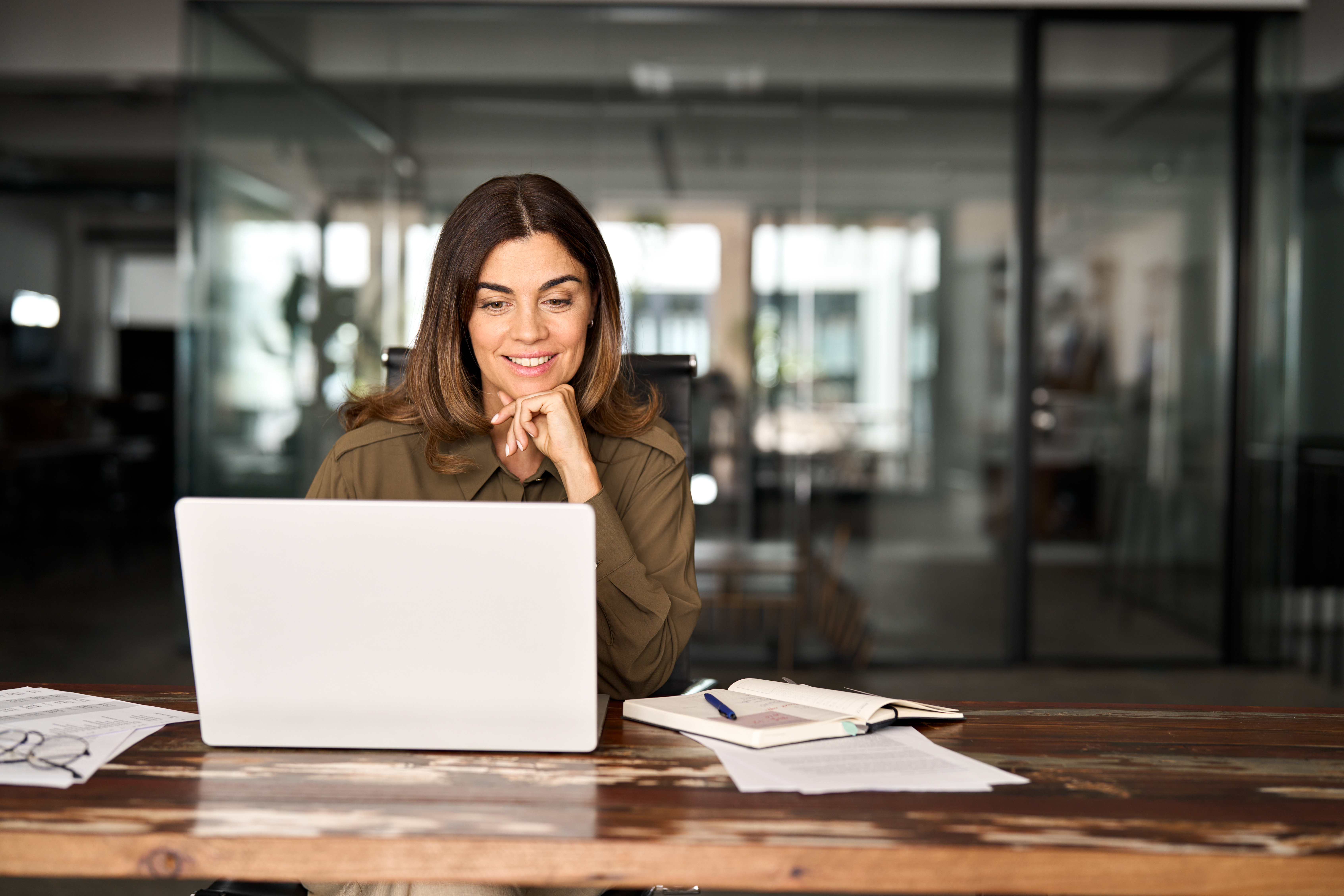 Woman sitting at a wooden desk using a laptop in a modern office