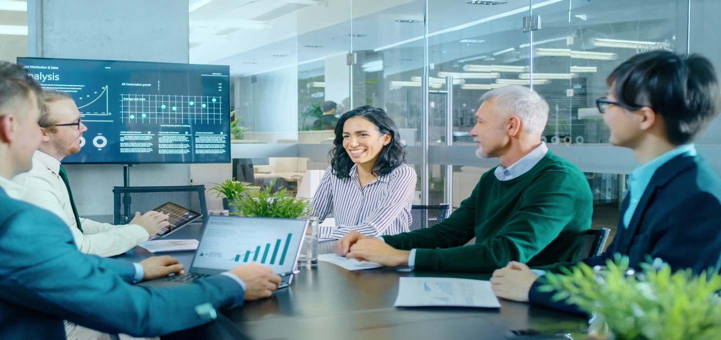 5 people in a meeting discussing data on a screen 