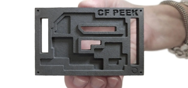 A hand holding a CF PEEK, CBAM part.