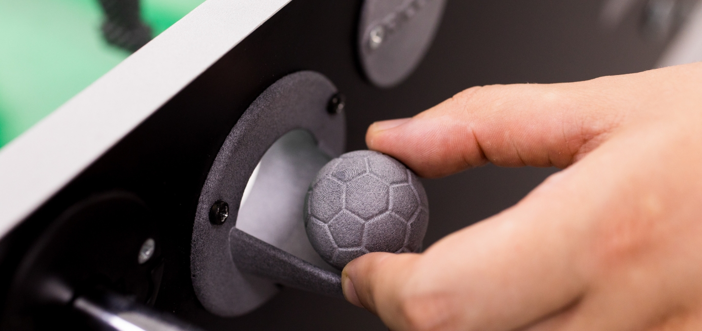 A hand placing a 3D-printed football into a table-football game.