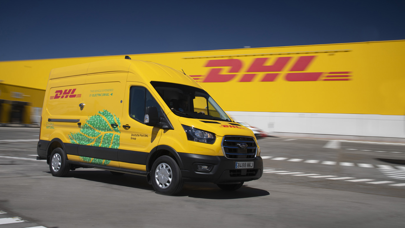 Yellow DHL delivery van driving outside a DHL facility, showcasing fast and reliable courier services.
